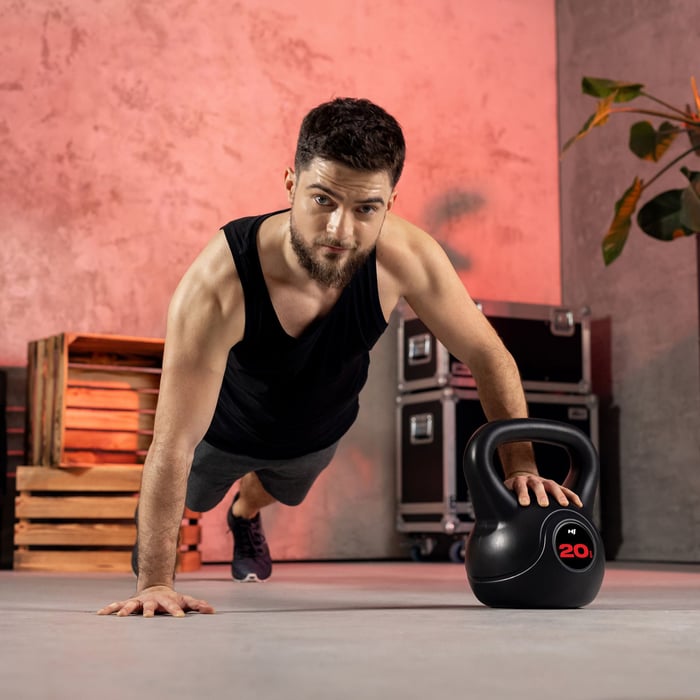 Man voert push-up uit op 20 kg kettlebell tijdens full-body workout.
