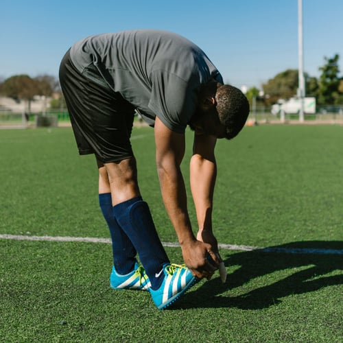 Man doet warming-up-oefeningen en strikt zijn schoenveter op het sportveld