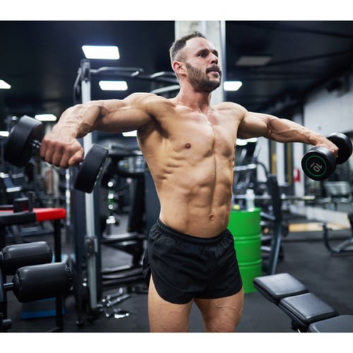 Shirtloze man traint schouders met dumbbells in de sportschool