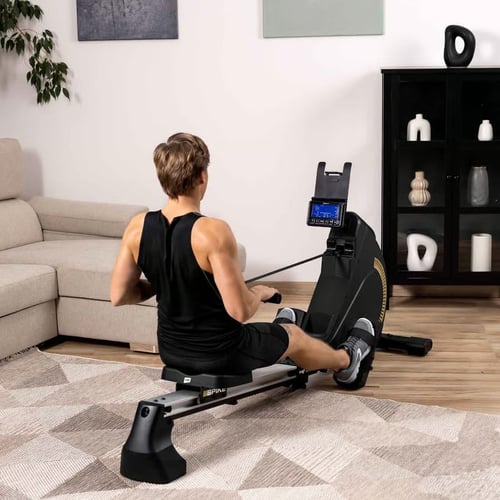 man van achteren gezien traint op een Hop-Sport roeitrainer op een vloerkleed