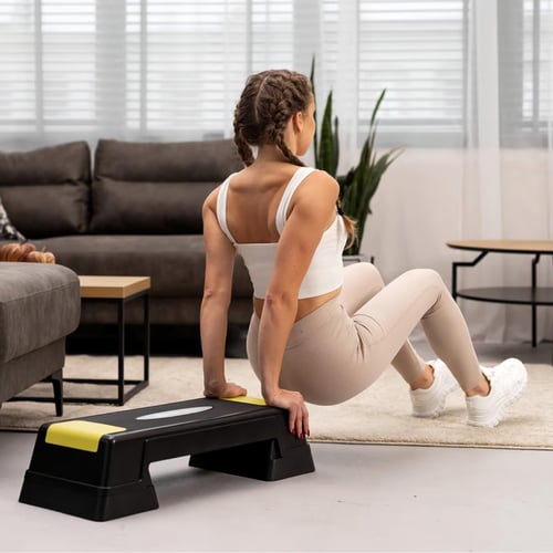 vrouw ontdekt de voordelen van aerobic step tijdens een push-up oefening met handen op een zwart-gele step in de woonkamer