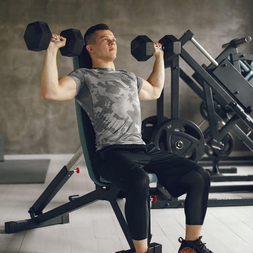Man voert schouderoefeningen met dumbbells uit op schuine bank