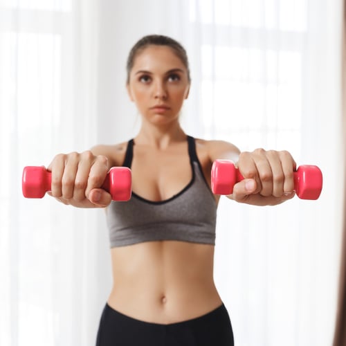 Vrouw houdt lichte dumbbells vast voor schouderoefeningen met dumbbells