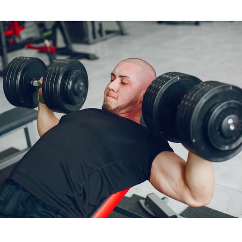 Man doet schouderoefeningen met dumbbells op de bank